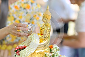 Songkran festival, Thai New Year. female hand holding silver bowl pouring water with jasmine and roses onto buddha statue