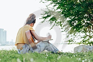 Songwriter create and writing notes,lyrics in the book on grass at parks beside the sea and building city background photo