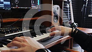 Songwriter musician engineer playing midi keyboard piano in home recording studio with monitors mixing gear and guitar. Home recor