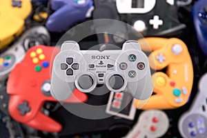A Sony Playstation Controller Hovering over a Pile of Retro Video Game Controllers