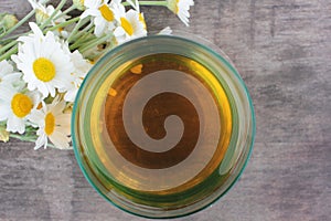 Soothing chamomile tea in a glass. Bouquet of daisy flowers on a wooden table. Top view