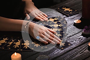 Soothsayer predicting future with tarot cards at table in darkness, closeup