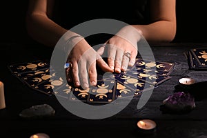 Soothsayer predicting future with tarot cards at table in darkness, closeup