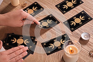 Soothsayer predicting future with tarot cards at wooden table, closeup