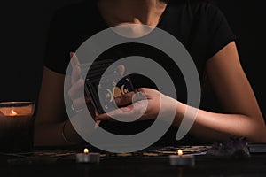 Soothsayer shuffling tarot cards at table in darkness. Fortune telling