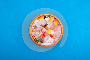 Sop Buah or Es Campur in clay plate on blue background, top view. Mixed fruit cocktail. Es buah Indonesian popular fruit ice with