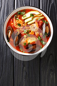 Sopa de Mariscos tomato soup with seafood and vegetables close-up in a bowl. Vertical top view
