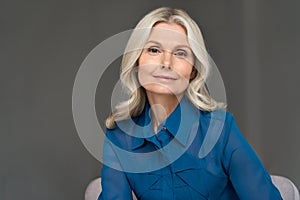 Sophisticated 50s middle aged woman model sitting in chair looking at camera.