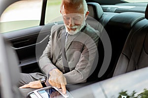 Sophisticated elder gentleman interacting with modern car dashboard during daytime drive