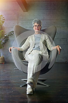 Sophisticated elegant beautiful 50s attractive middle aged smiling woman model sitting in chair looking at camera at