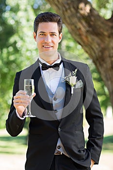 Sophisticated groom holding champagne flute in garden