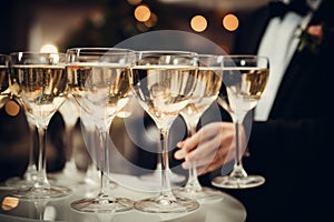 A sophisticated man dressed in a formal tuxedo holds a tray filled with sparkling champagne glasses, Cocktail glasses filled with