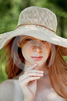 A sophisticated red-haired girl in a simple linen dress, in a light wide-brimmed hat.Model look. Natural beauty