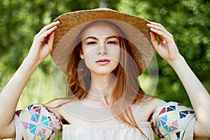 A sophisticated red-haired girl in a simple linen dress, in a light wide-brimmed hat.Model look. Natural beauty