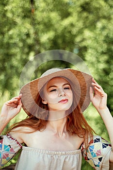 A sophisticated red-haired girl in a simple linen dress, in a light wide-brimmed hat.Model look. Natural beauty