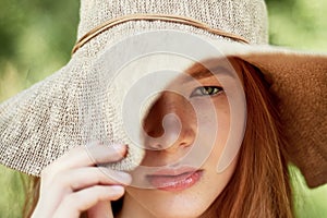 A sophisticated red-haired girl in a simple linen dress, in a light wide-brimmed hat.Model look. Natural beauty