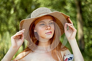 A sophisticated red-haired girl in a simple linen dress, in a light wide-brimmed hat.Model look. Natural beauty