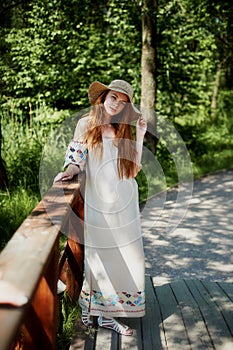 A sophisticated red-haired girl in a simple linen dress, in a light wide-brimmed hat.Model look. Natural beauty