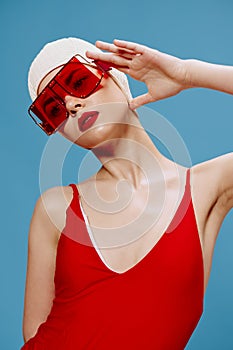 A sophisticated red-lipped lady in a swimming cap and a red swimsuit touches her glasses and looks aside posing on a