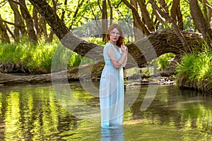 The sorceress women stands in a blue dress inside the river