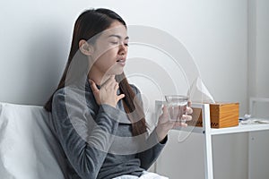 Sore throat in flu season. Young woman touching her neck and feeling pain in throat in the bedroom at home