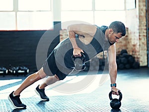 Sore today, strong tomorrow. Shot of a young man doing push ups with kettlebells in a gym.