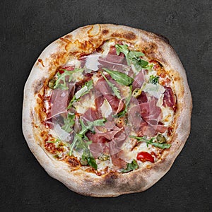 Sorrentina pizza with prosciutto, arugula, capers, pelati sauce, pesto. Neapolitan round pizza on dark background