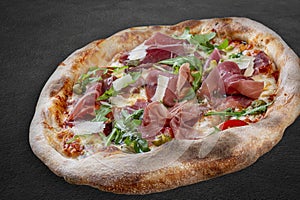 Sorrentina pizza with prosciutto, arugula, capers, pelati sauce, pesto. Neapolitan round pizza on dark background
