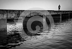 Sorrow. Silhouette of a lonely man on a pier, black and white image.