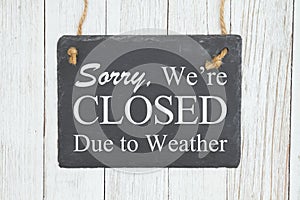 Sorry we`re Closed Due to weather text on a hanging chalkboard on weathered whitewash textured wood