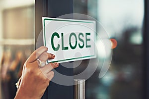 Sorry, were closed. Closeup shot of a young business owner hanging up a close sign on the door of her shop.