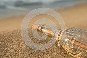 SOS message in glass bottle on sand, closeup