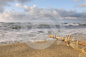 SOS message in glass bottle on sand near sea, closeup. Space for text