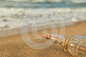 SOS message in glass bottle on sand near sea, closeup. Space for text