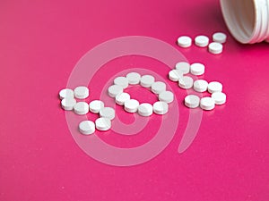 SOS word made of pills and capsules on a pink background. Pills on a blue background