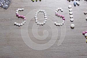 SOS word made of pills on a wooden table. Different pills and blister packs