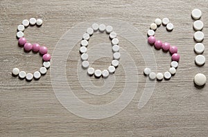 SOS word made of pills on a wooden table. Different pills and blister packs