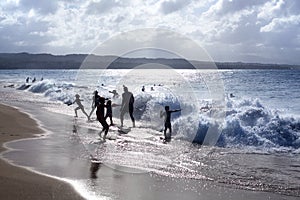 Silhouettes of children and people playing on the beach in the waves and water splashes on vacation, blue sea, waves sun light