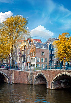 Soul of Amsterdam is leaning houses, bridges, canals. Beautiful autumn, golden falling leaves and blue sky. Autumn day in