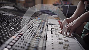 Sound engineer is moving levers of a multitrack mixing console in the control room during a recording session