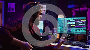 Sound engineer playing acoustic guitar and using mixing console to record music