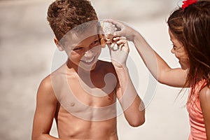 Sounds of the sea. a little girl holding a conch shell against her brothers ear.