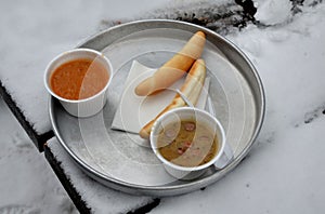 Soup on an aluminum tray in a polystyrene bowl with plastic cutlery and a croissant on a wooden table in winter on skis will save