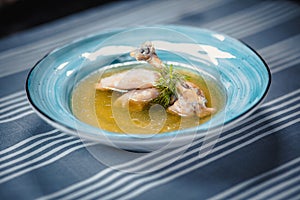 Soup in blue plate with chicken broth, chicken`s leg, dumplings and greenery. Plate on the table with a blue tablecloth