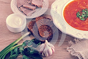 soup in a bowl with dill, sour cream, beef and black bread on wooden background