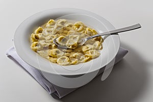 Soup bowl with tortellini in broth with spoon
