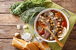 Soup of chickpeas, kale, tomatoes, garlic and potatoes with lemon close up on the table. Horizontal top view