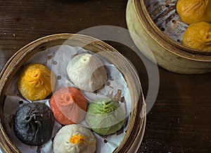 soup dumplings in a bamboo steam tray on wooden table (Xiaolongbao, xiao long bao) pork, colorful dough Shanghai