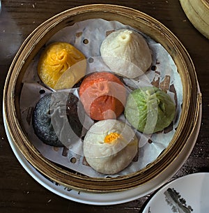 soup dumplings in a bamboo steam tray on wooden table (Xiaolongbao, xiao long bao) pork, colorful dough Shanghai