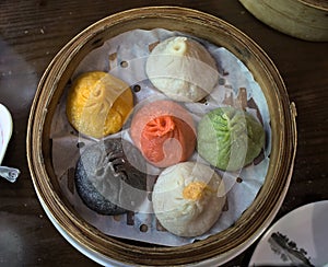soup dumplings in a bamboo steam tray on wooden table (Xiaolongbao, xiao long bao) pork, colorful dough Shanghai